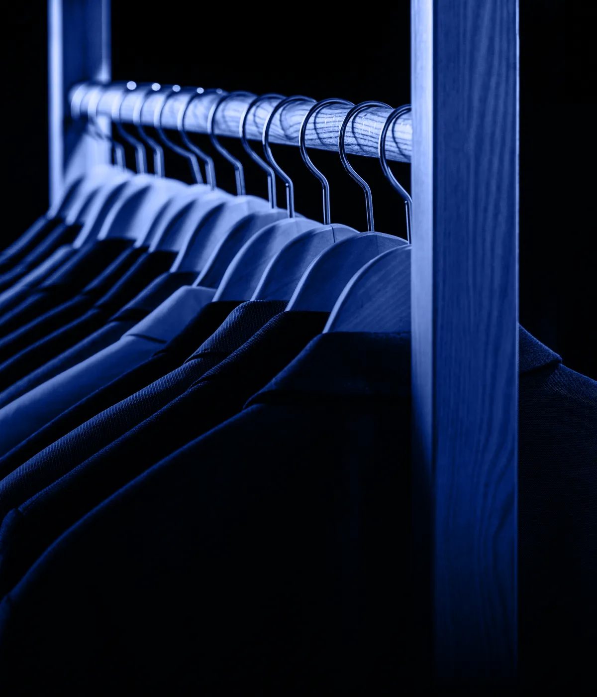 Ряд мужских пиджаков на деревянных плечиках в гардеробе